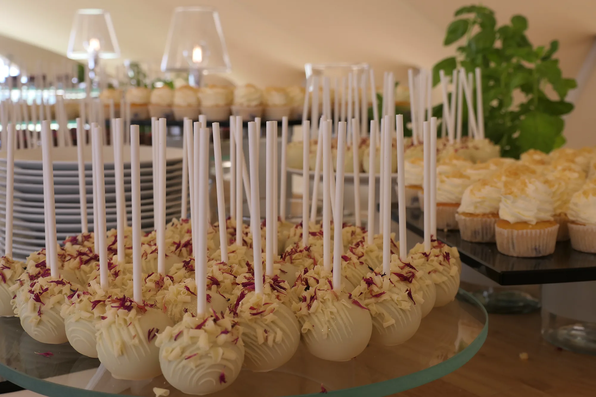 Cake pops v bílé čokoládě a cupcakes na patrovém dezertovém stole